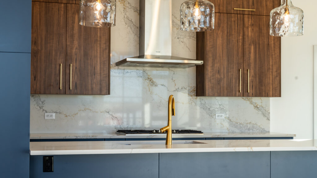 Great backsplash with clean modern look. The marble has gold veining with light cream color stone. Brown and blue cabinets with Gold faucet.